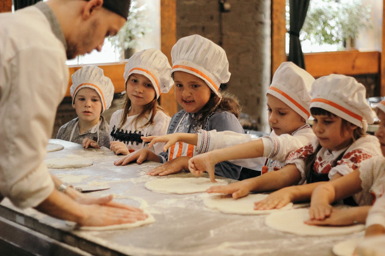 my-qualifications Group of children learning to bake pizza at a restaurant kitchen under a chef's guidance.
