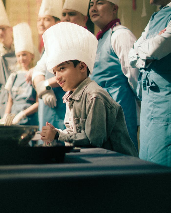 contact-img A young boy in a chef hat participates in a lively cooking class with instructors.